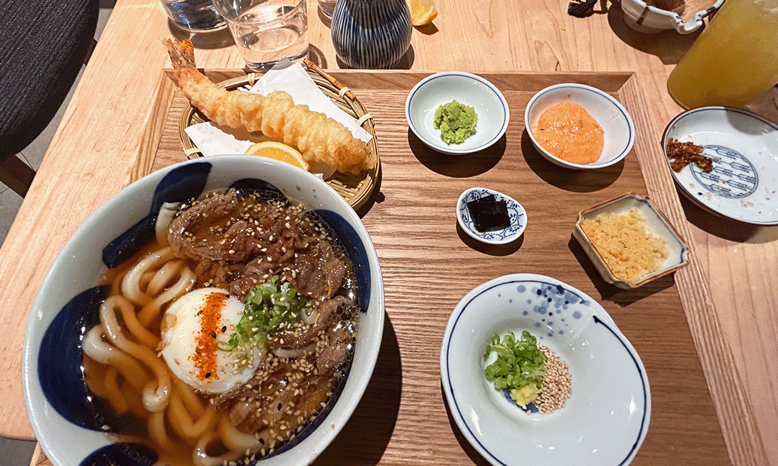 bowl of udon and meat with small dishes of toppings